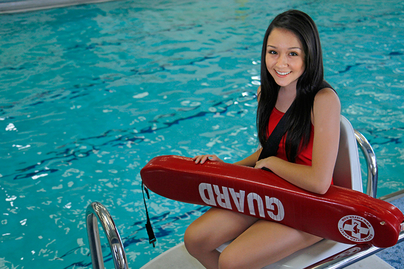 Lifeguard sits in front of a pool wearing a red suit