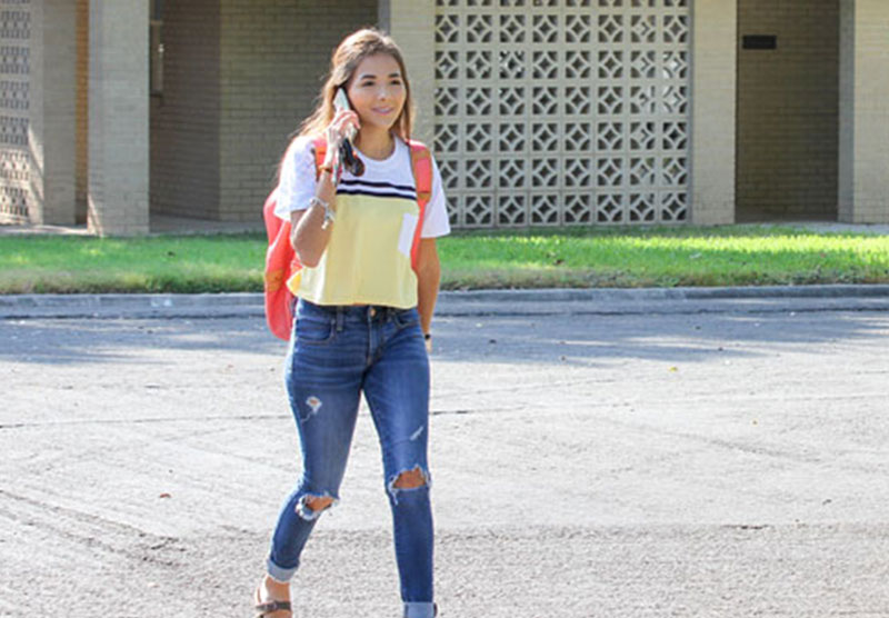 female student walking across campus on cell phone