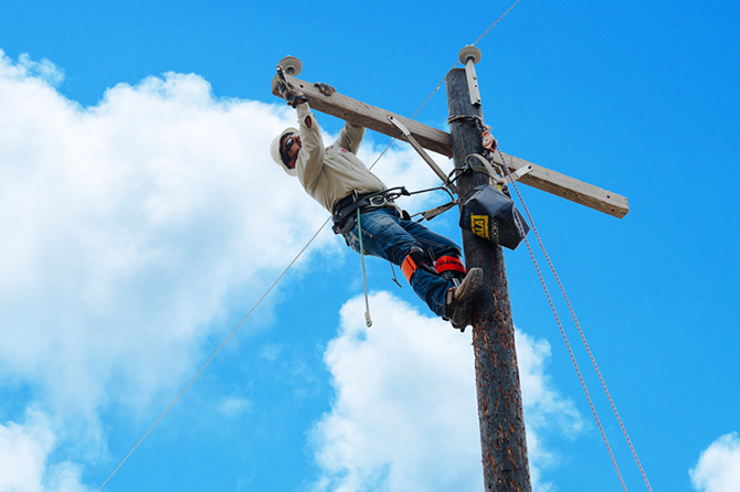 Lineman inspecting the wiring on a pole while secured to safety equipment.