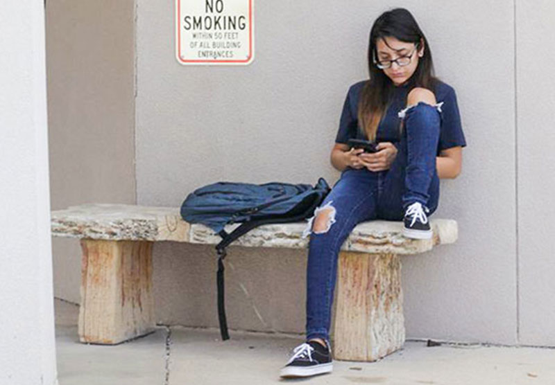 female student sitting on an outdoor bench looking at cellphone