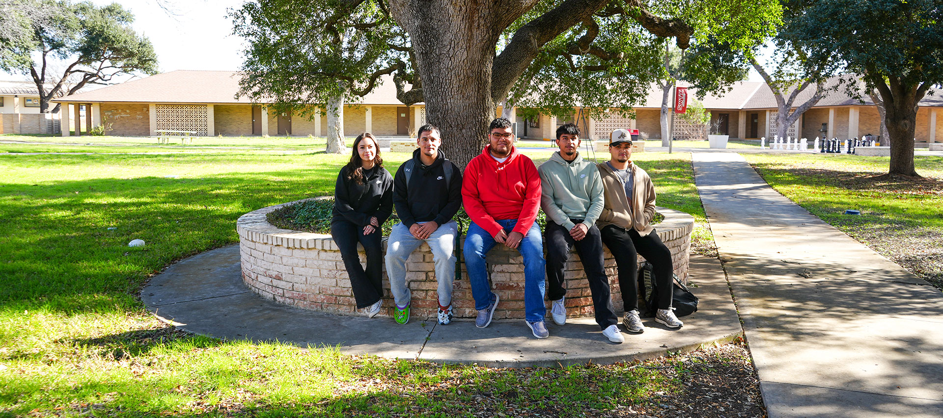 Students sitting on a brick tree ring in the courtyard of the Uvalde campus.